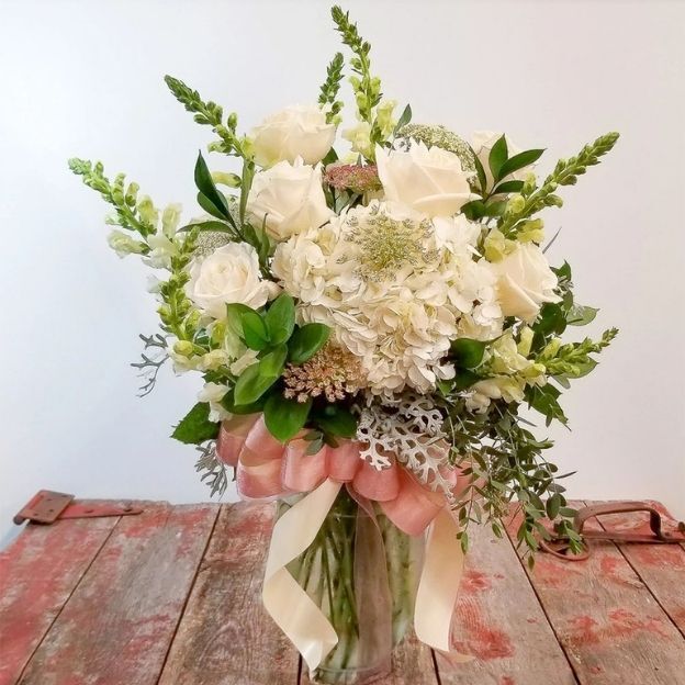Elegant ivory roses, hydrangea, and alstroemeria with greenery in a tapered glass vase, finished with a pink bow.