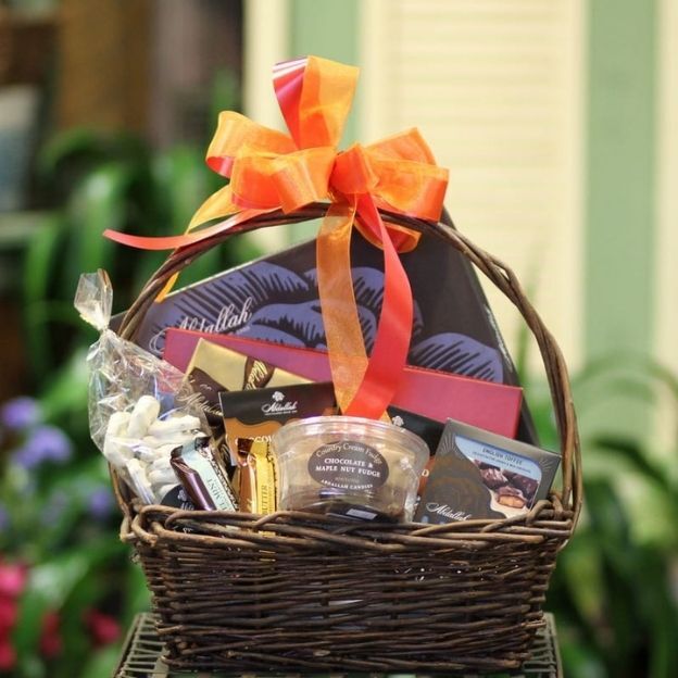 Gift basket filled with assorted chocolates and treats, wrapped with clear cellophane and an orange ribbon.