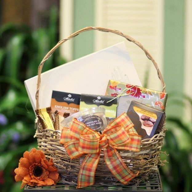 Wicker gift basket with gourmet chocolates, a greeting card, and an orange plaid bow.