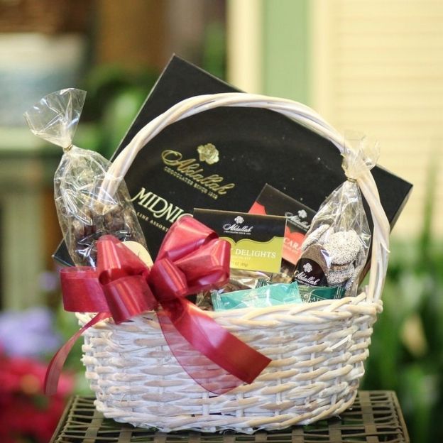 White wicker gift basket filled with gourmet chocolates and treats, decorated with a red ribbon.