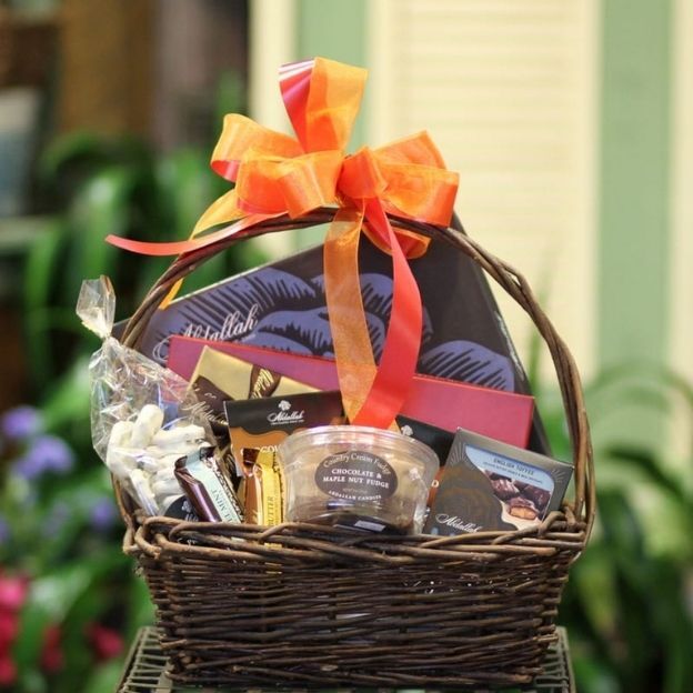 Assorted gourmet chocolate gift basket in a brown wicker handle, decorated with a bright orange ribbon.